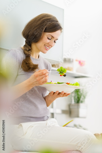 Photo: Smiling young woman eating salad and talking mobile phone Smiling young woman eating salad and talking mobile phone
