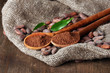 Cocoa powder in spoons and cocoa beans on wooden background