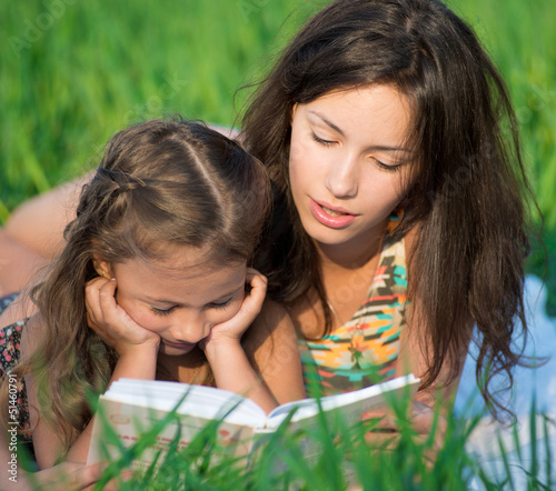 Photo: Happy girls reading book on green grass Happy girls reading book on green grass
