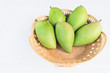green mangoes in a plastic wooden basket on white background