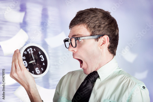 Photo: Stressed male office worker holding overtime clock Stressed male office worker holding overtime clock