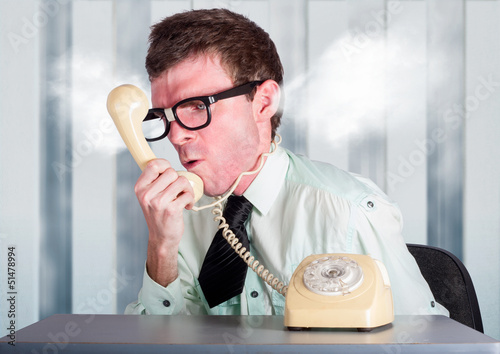 Photo: Unhappy nerd businessman yelling down retro phone Unhappy nerd businessman yelling down retro phone