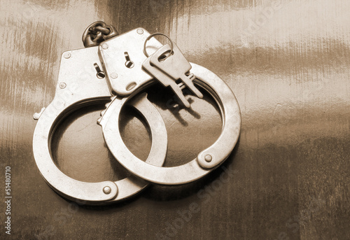 Photo: Steel metallic handcuffs with keys on wooden table Steel metallic handcuffs with keys on wooden table