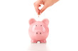 Female hand putting a coin into piggy bank