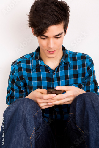 Photo: Young man looking at his smart phone while text messaging Young man looking at his smart phone while text messaging