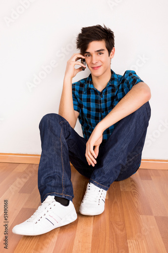 Photo: Young man talking on the phone at home Young man talking on the phone at home