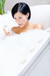 Woman taking a bath with suds and candles drinks fizz 