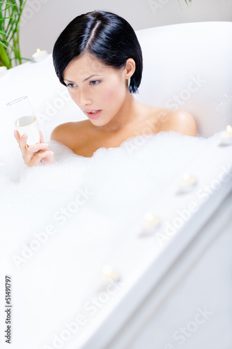 Photo: Woman taking a bath with suds and candles drinks fizz Woman taking a bath with suds and candles drinks fizz