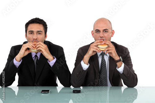 Photo: Two businessmen enjoying a burger. Two businessmen enjoying a burger.