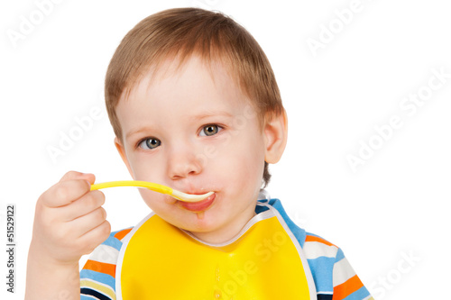 Photo: Boy eats with a spoon puree, isolated on white Boy eats with a spoon puree, isolated on white