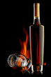 Bottle and glass of cognac over dark background with flame