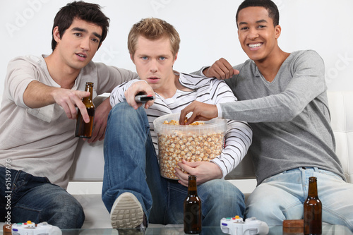 Photo: Three male friends watching television together Three male friends watching television together