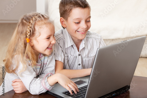 Photo: Happy kids playing laptop at home Happy kids playing laptop at home