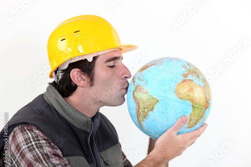 Photo: A construction worker kissing a globe. A construction worker kissing a globe.