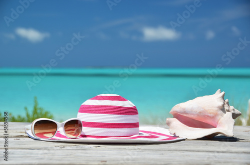Photo: Sunglasses, hat and shell against ocean. Exuma, Bahamas Sunglasses, hat and shell against ocean. Exuma, Bahamas