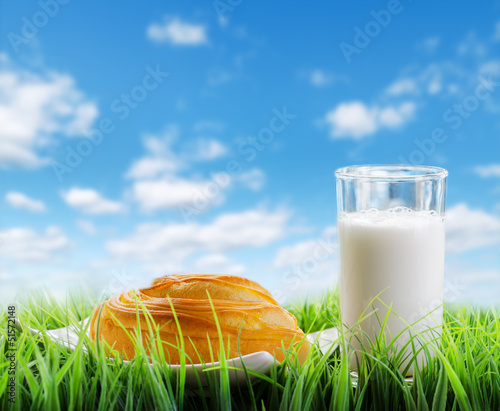 Photo: Fresh cinnamon bun and glass of milk on sky background Fresh cinnamon bun and glass of milk on sky background