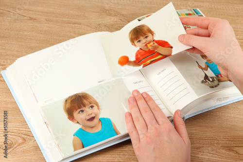 Photo: Photos in hands and photo album on wooden table Photos in hands and photo album on wooden table