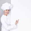 Female chef cook shows a blackboard with copyspace