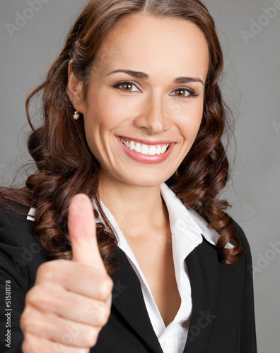 Photo: Businesswoman with thumbs up, over grey Businesswoman with thumbs up, over grey