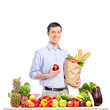 Smiling man holding an apple and bag with food products, posing