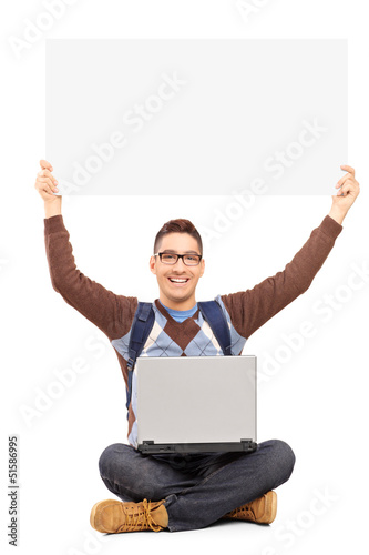Photo: Smiling male student sitting with laptop and holding a blank pan Smiling male student sitting with laptop and holding a blank pan