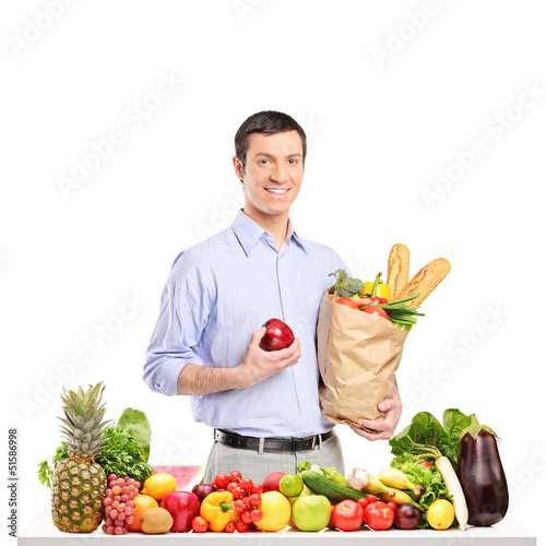 Photo: Smiling man holding an apple and bag with food products, posing Smiling man holding an apple and bag with food products, posing