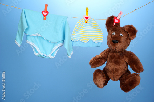 Photo: Baby clothes hanging on clothesline, on blue background Baby clothes hanging on clothesline, on blue background