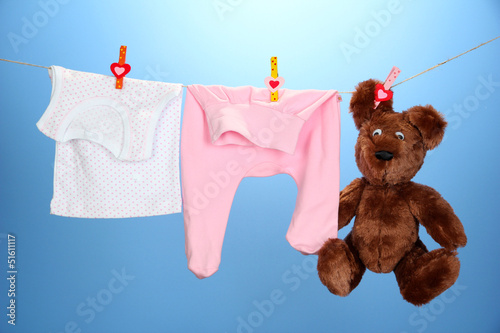 Photo: Baby clothes hanging on clothesline, on color background Baby clothes hanging on clothesline, on color background