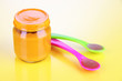 Baby food with weaning spoons on yellow background