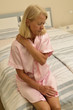 Seniorin sitzt auf einem Bett mit Schulterverspannung