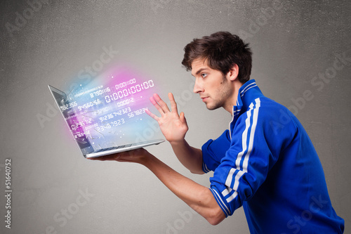 Photo: Casual man holding laptop with exploding data and numbers Casual man holding laptop with exploding data and numbers