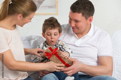 Photo: Couple giving gift to their little son in the living room. Happy Couple giving gift to their little son in the living room. Happy