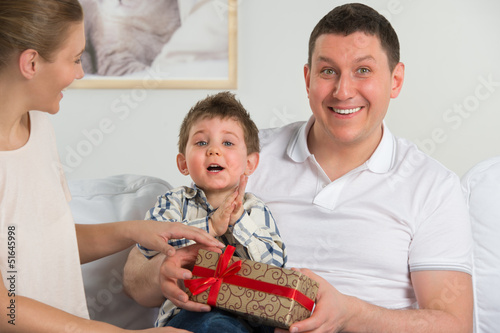 Photo: Couple giving gift to their little son in the living room. Happy Couple giving gift to their little son in the living room. Happy
