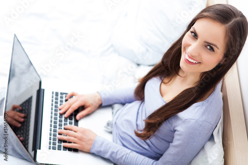 Photo: Woman sitting on bed with laptop Woman sitting on bed with laptop