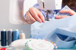 Hands on sewing machine with reels of colour threads and sewing
