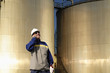 worker talking in phone with fuel tanks in background