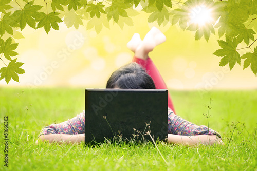 Photo: Asian student looking at laptop on green grass Asian student looking at laptop on green grass