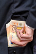 Business man putting bribe money in his pants back pocket.