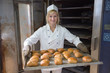 Baker in bakehouse or bakery putting bread in the oven