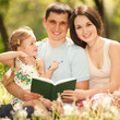 Happy mother, father and daughter read a book in the park