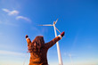 Happy woman with hands up looking at eco wind turbines