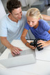 Father and daughter looking at digital camera and laptop