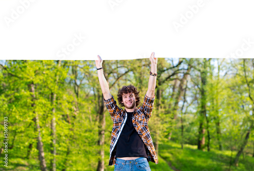 Photo: Young man holding a huge blank paper in nature Young man holding a huge blank paper in nature