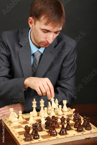 Photo: Young business man playing chess on black background Young business man playing chess on black background