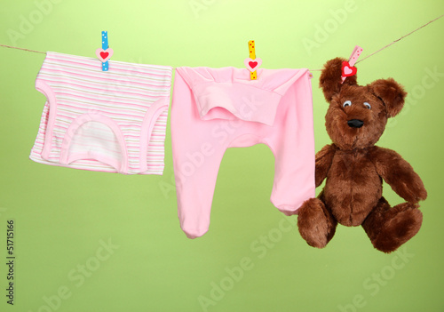 Photo: Baby clothes hanging on clothesline, on color background Baby clothes hanging on clothesline, on color background
