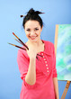 Beautiful young woman painter at work, on color background
