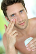 Handsome man applying moisturizing cream