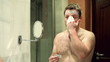 Vídeo: Young man applying face mask in front of mirror Young man applying face mask in front of mirror