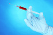 Hand holding syringe filled with blood on blue background