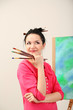 Beautiful young woman painter at work, on color background